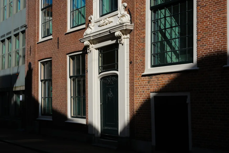 Bakstenen gevel met een wit geschilderde deuromlijsting en houten ramen